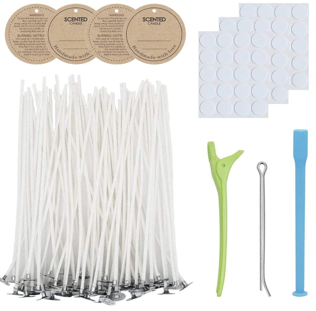 This candle-making kit features essentials for crafting candles with dried flowers, including numerous white wicks with metal bases, four brown circle labels, a green wick holder, a blue wick centering tool, a silver needle tool, and adhesive dots on sheets.